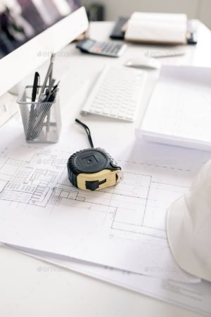 Measuring tape, pencils and blueprints with sketches on workplace of contemporary engineer in office